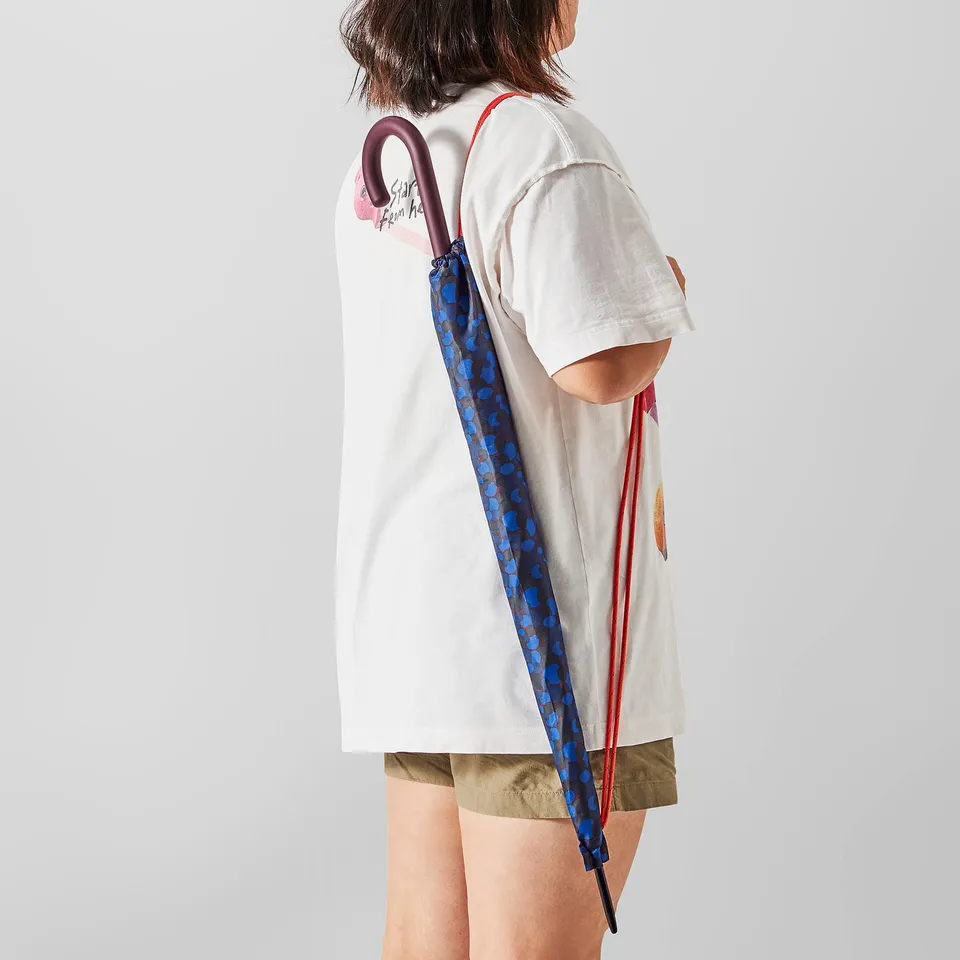 Person holding colourful polka-dot umbrella over shoulder, wearing a white t-shirt with heart design.