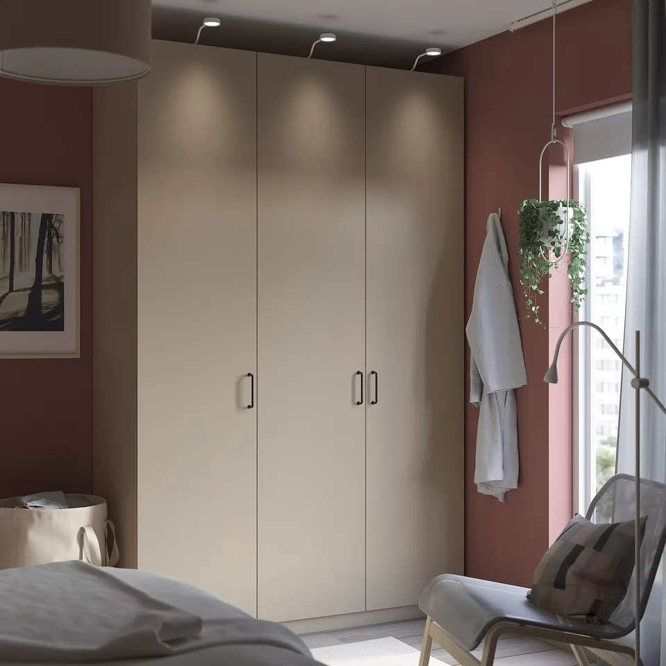Modern bedroom with large wardrobe, light grey bedding, red walls, hanging plant, and a picture frame.