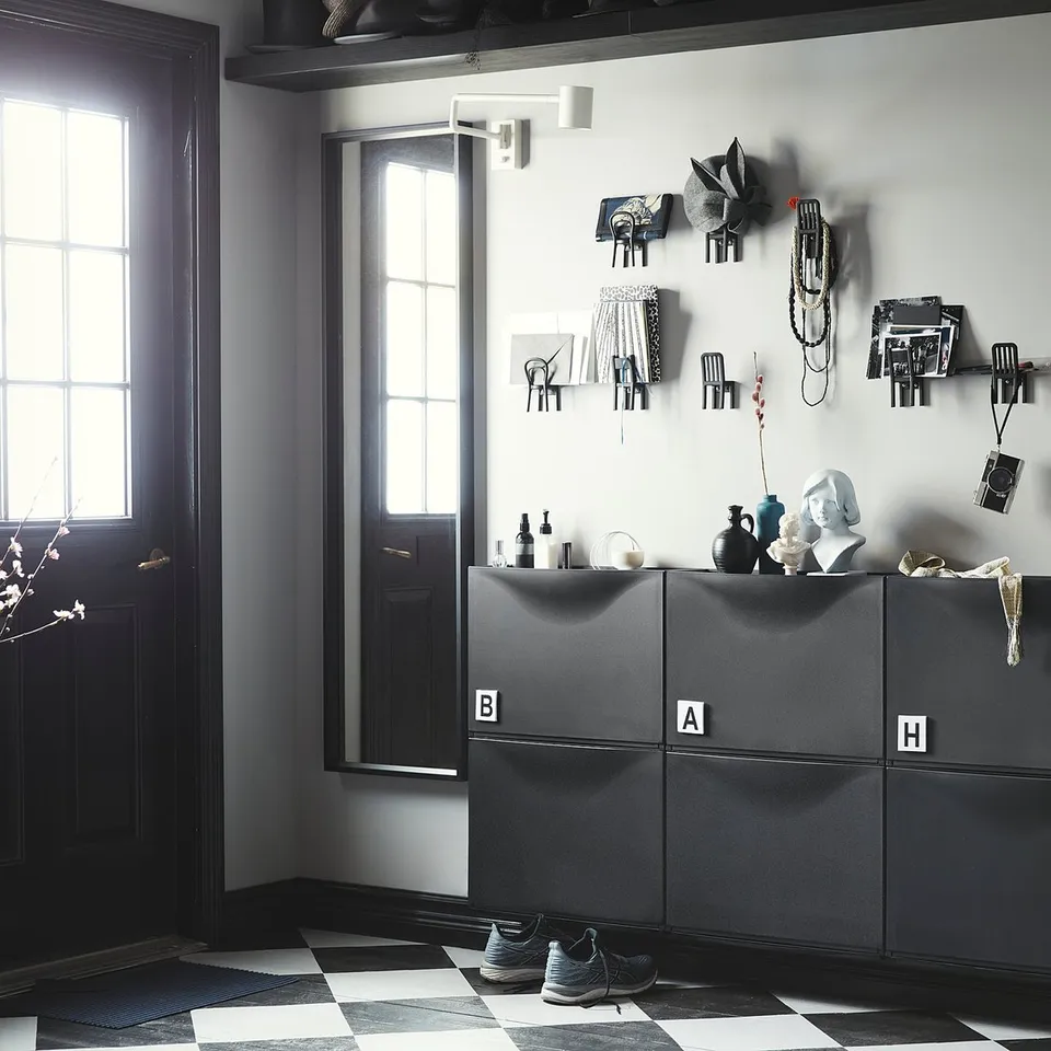 Modern entryway with black/white decor, grey storage, wall hooks, chequered floor, black door, plant.