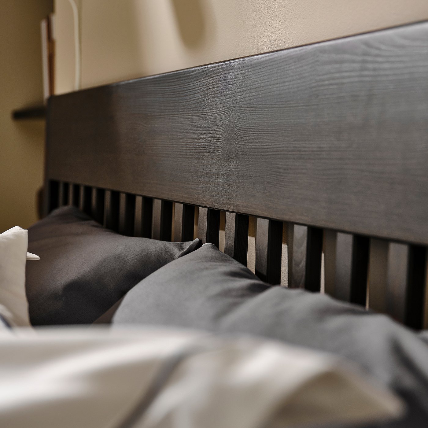 Grey wooden bed frame with dark bedding.