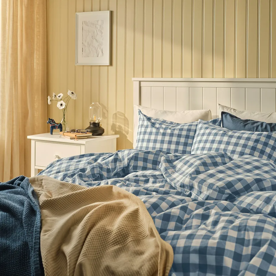 Cosy bed with blue-white chequered EKTANDVINGE duvet set, made of 100% organic cotton, fitting neatly against a wooden headboard.