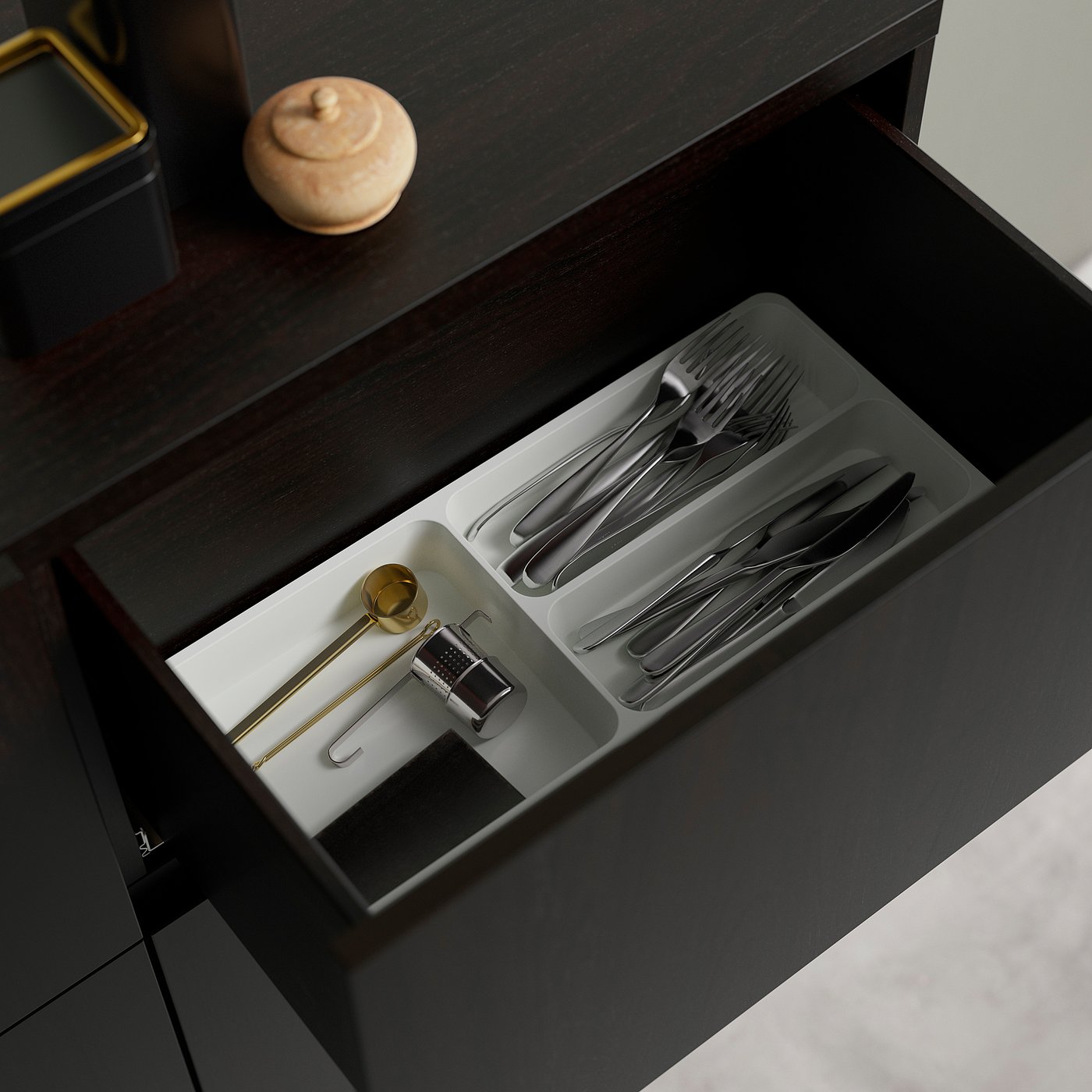 Open drawer of dark wood sideboard displaying neatly organised utensils in compartments.