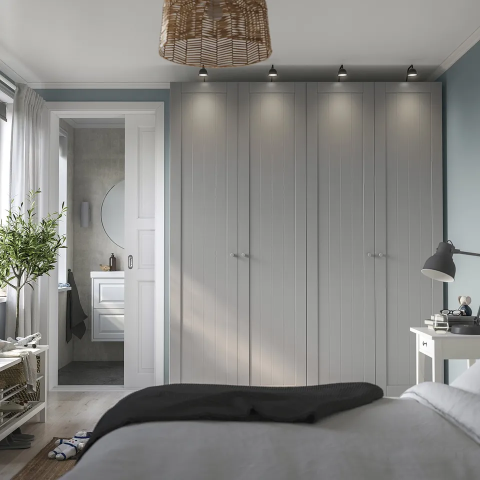 Modern grey GULLABERGet wardrobe beside white door with black lamp on white table. Wooden floor with natural light from left.