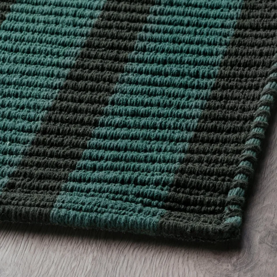 Green and black striped rug on wood floor. Soft, braided texture.