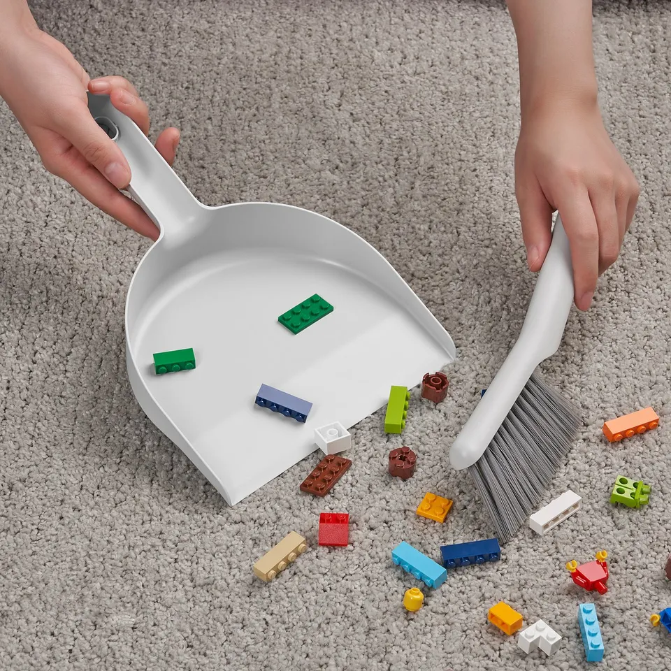 Child cleaning scattered toys with dustpan and brush, demonstrating its use for tidying.