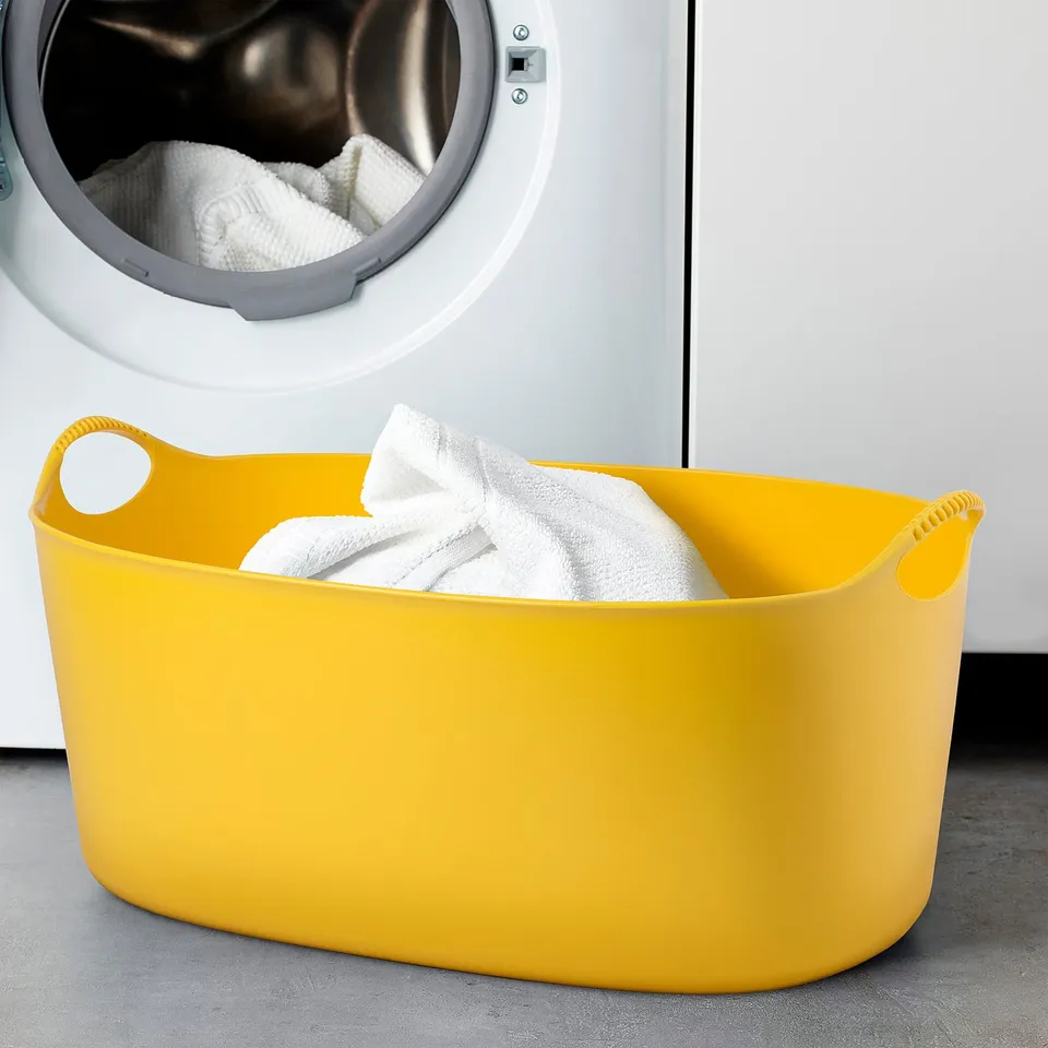 Bright yellow TORKIS laundry basket with white towels, perfect for carrying laundry.
