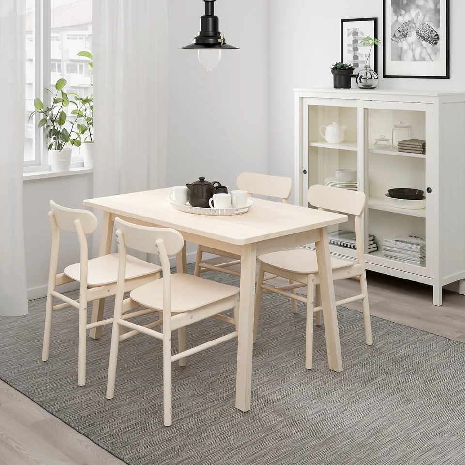 Wooden dining set with square table & curved chairs near window with plant.