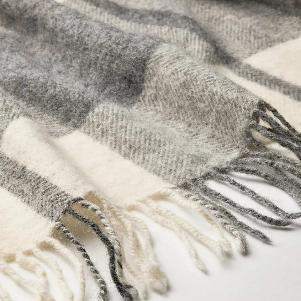 Grey and white chequered wool throw blanket with frayed edges, showcasing its soft, thick texture.