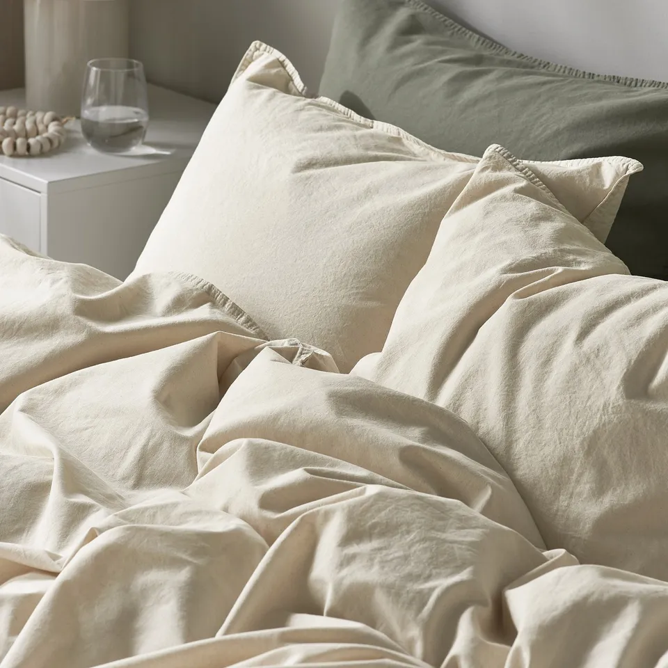 A neatly made bed with plain, off-white bedding. Soft, natural cotton duvet cover and pillowcases.