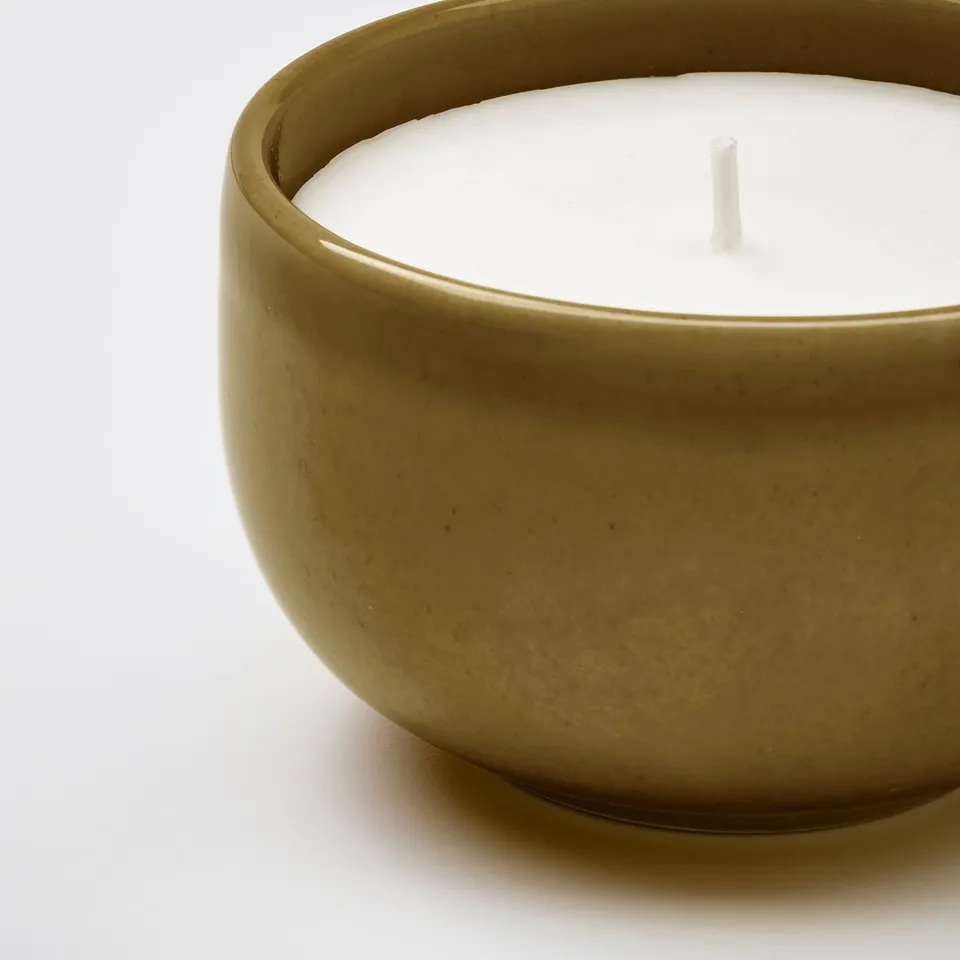 Close-up of a green, handcrafted stoneware candle with white wax and a wick, showcasing its rustic, artisanal quality.