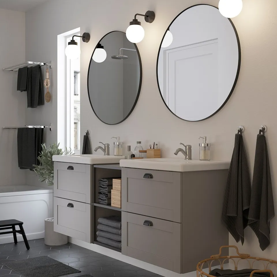 Modern bathroom with large mirrors above twin sinks, soft lighting, dark frames, and hanging towels.