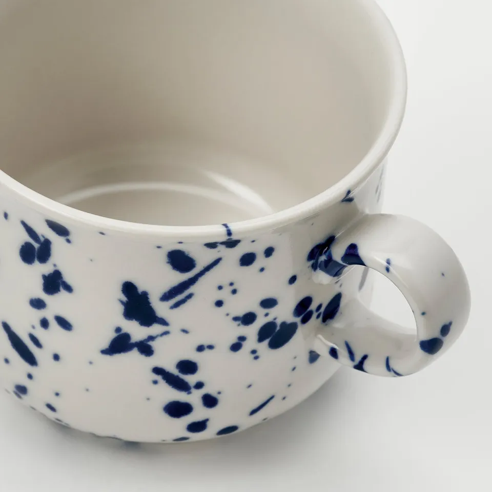 White mug with blue speckles, smooth handle, elegant design.