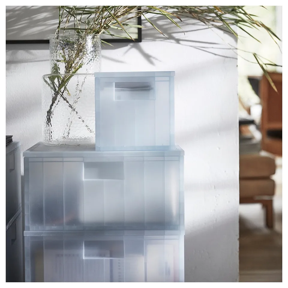 Stacked transparent PANSARTAX boxes with plant vase indoors.