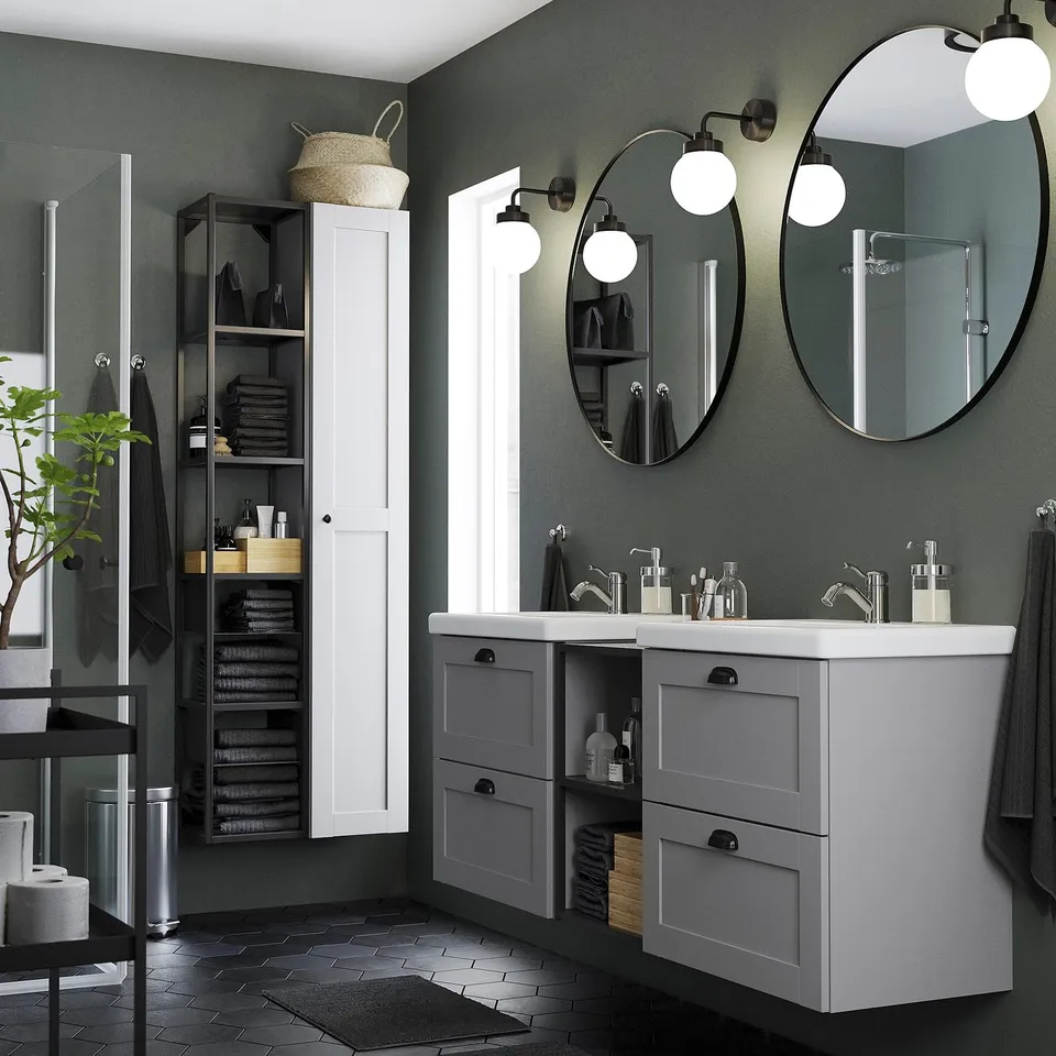 Modern bathroom with dual vanity, round mirrors, and white countertop, featuring black and grey accents, including a tall white cabinet.