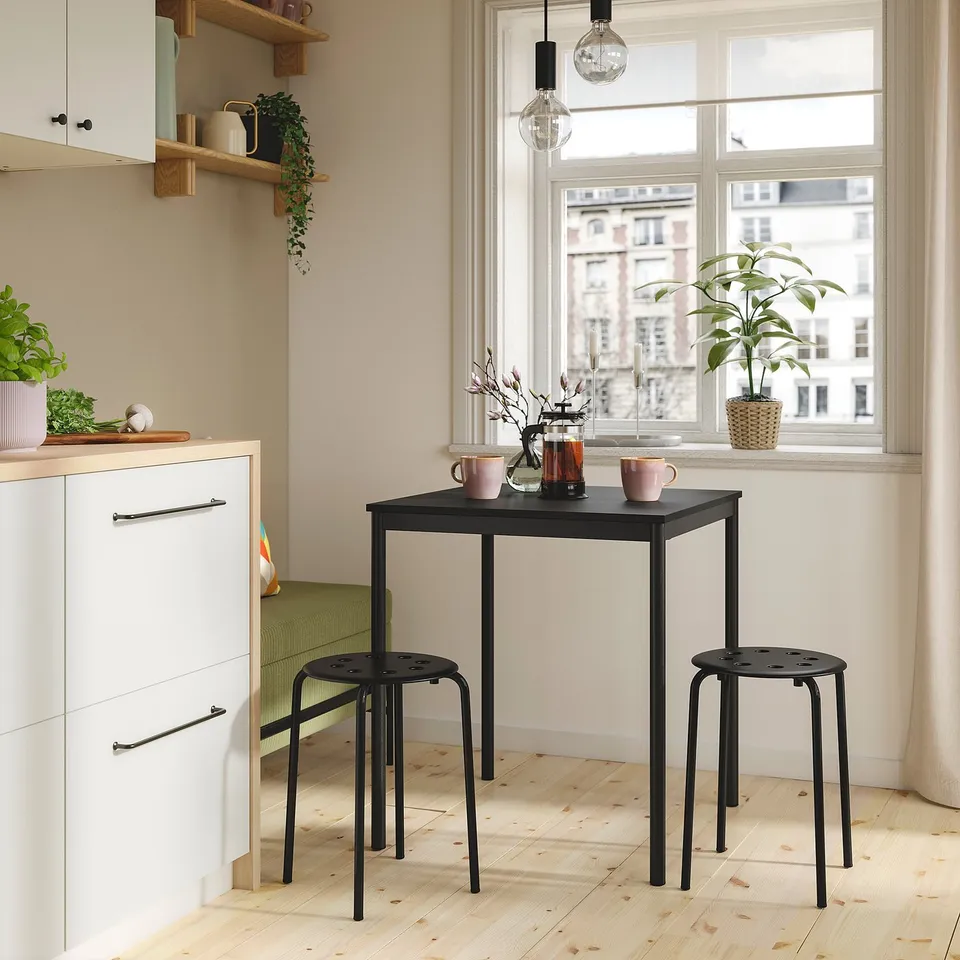 Small black sandberg table and stools near white kitchen cabinets, bright window, modern design.