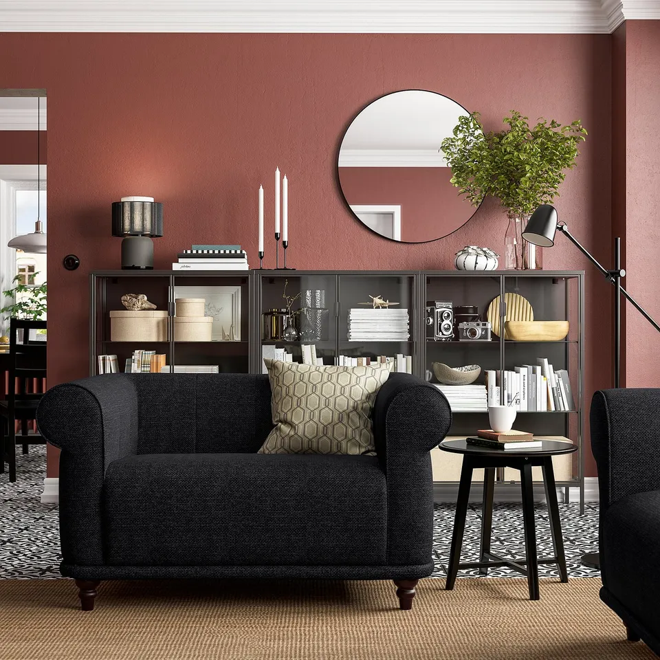 Cosy living room with dark grey VISKAFORS armchair, geometric pillow, and black bookshelf against red walls.