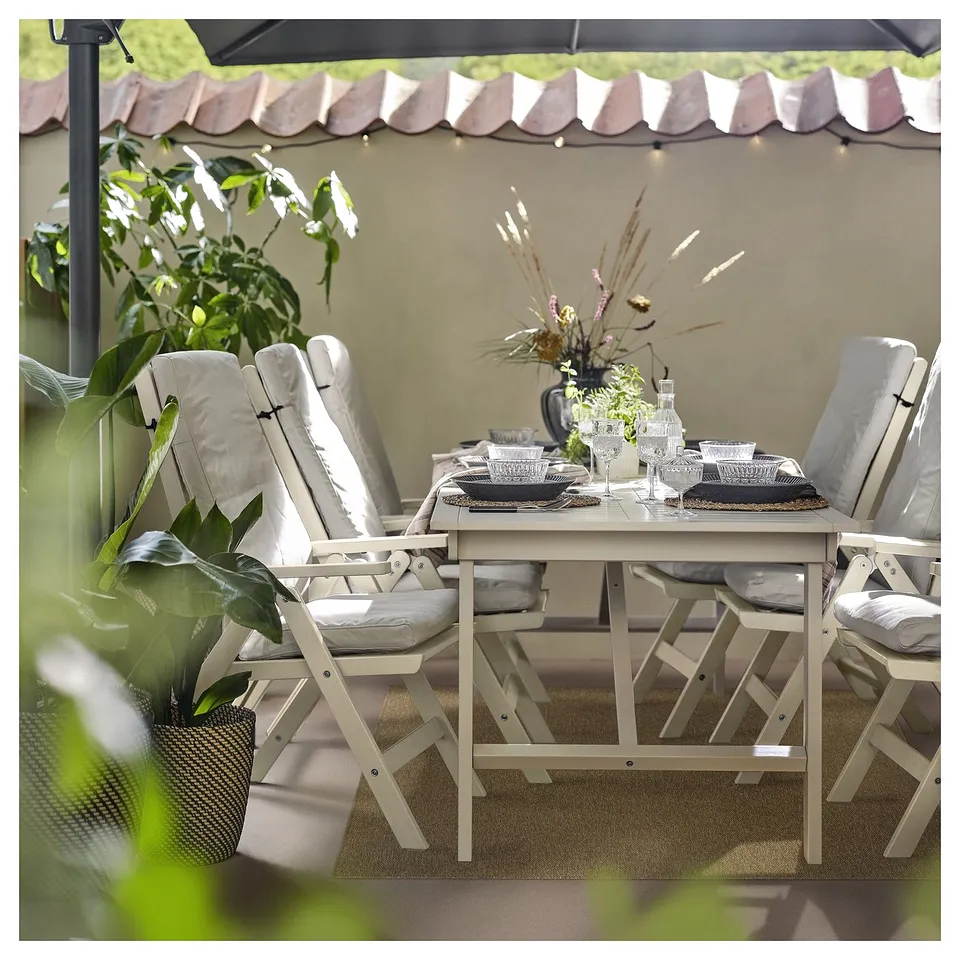 Outdoor seating area with white chairs, beige table, and decorated with plants.
