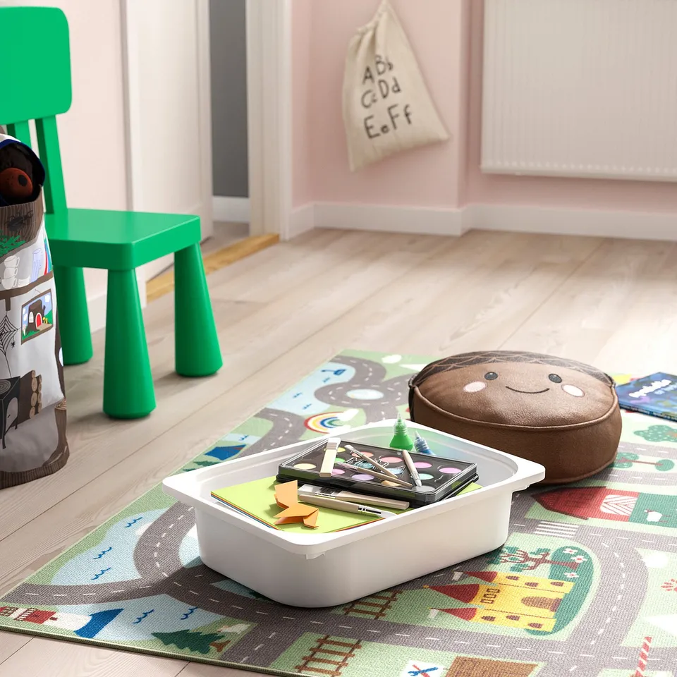 Childs play area with green chair, soft toy, and container of art supplies on a colourful mat.