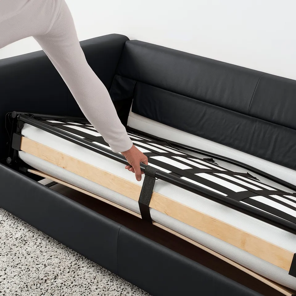 Person adjusts strap on black VIMLE sofa-beds mechanism, showing its convertible functionality.