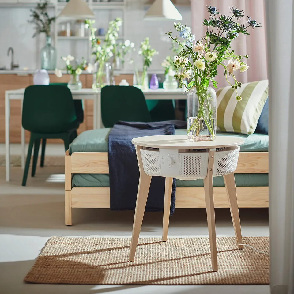 Modern living room with ikea STARKVIND air purifier, flowers, green chairs, cozy sofa, pillows, and blue blanket.