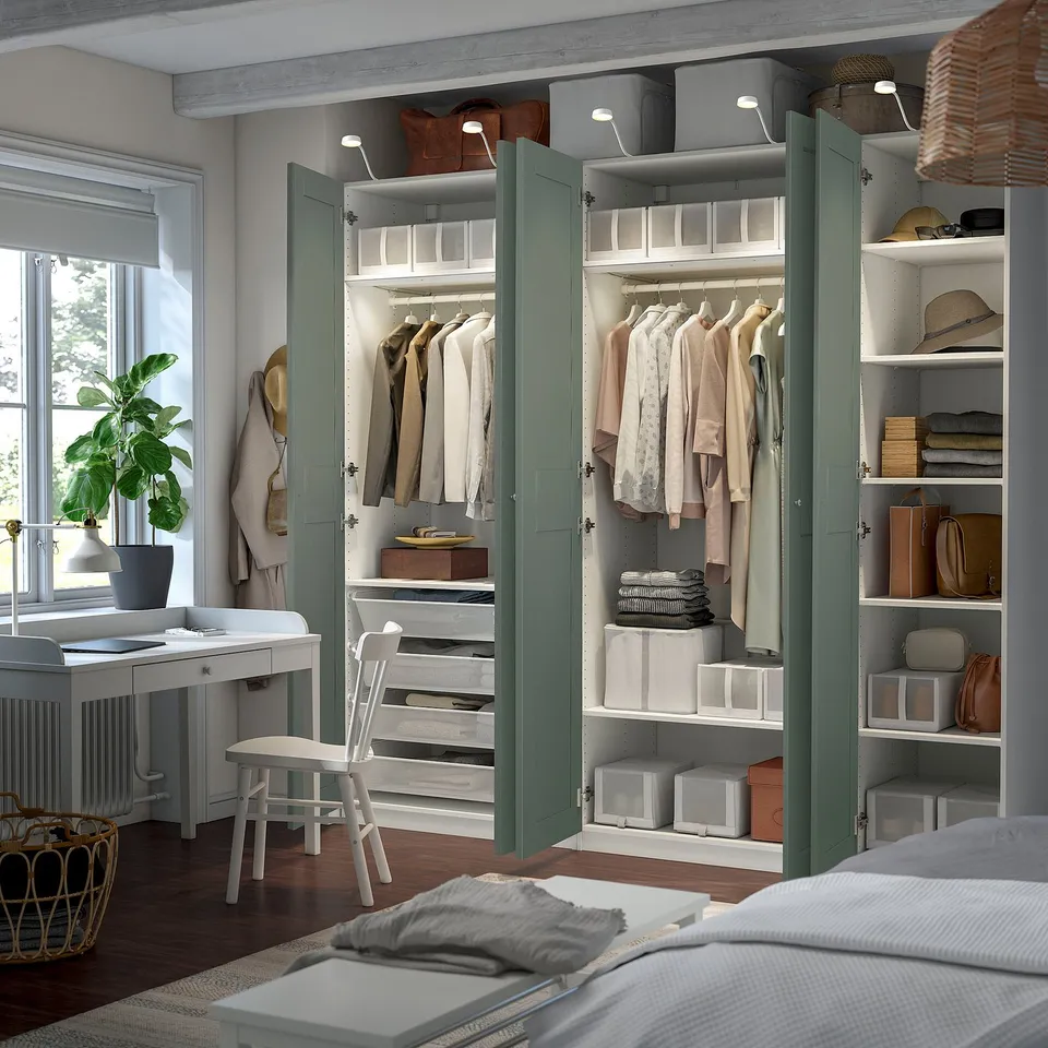 Open wardrobe with clothes and shelves, integrated lighting, and a desk with a plant beside it.