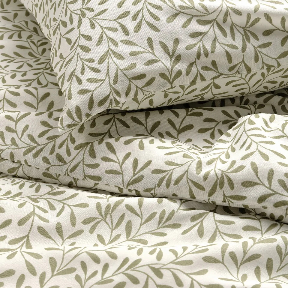 Stacked white duvet cover and pillowcases with subtle green leaf patterns, showcasing high-quality fabric texture.
