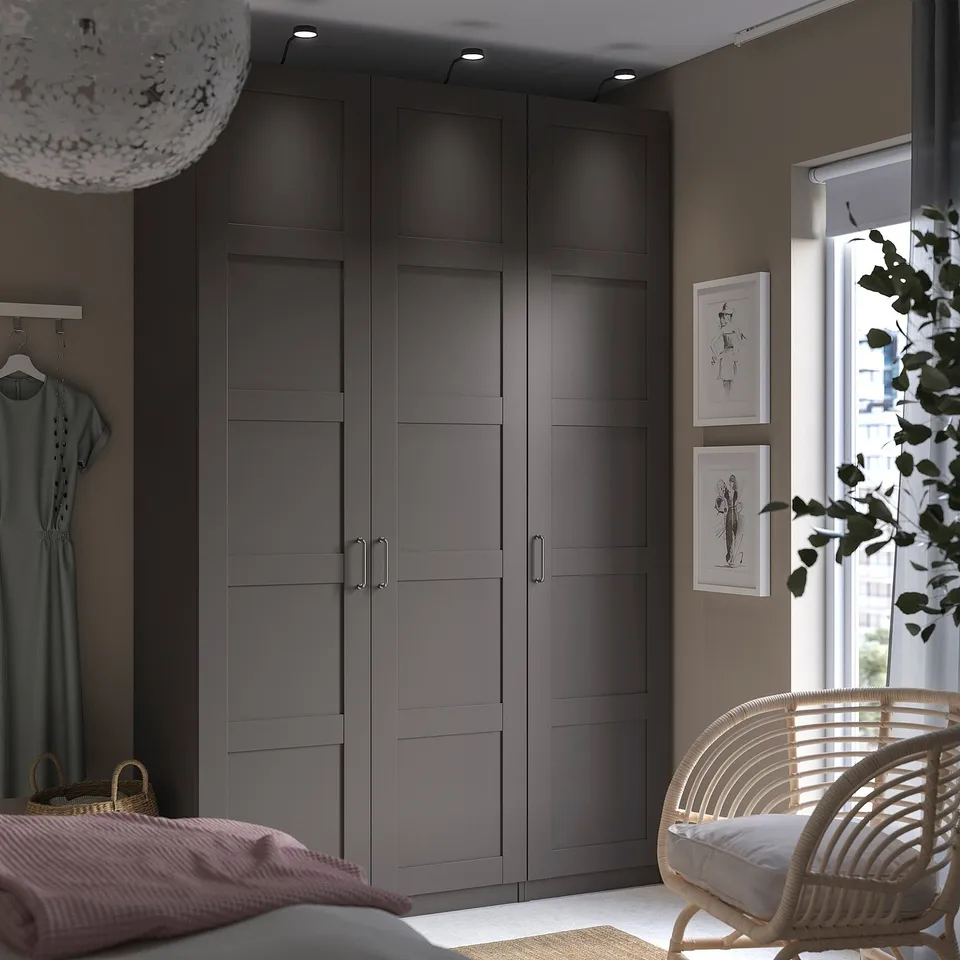 Modern bedroom with tall grey BERGSBO wardrobe, wicker chair, and hanging light.