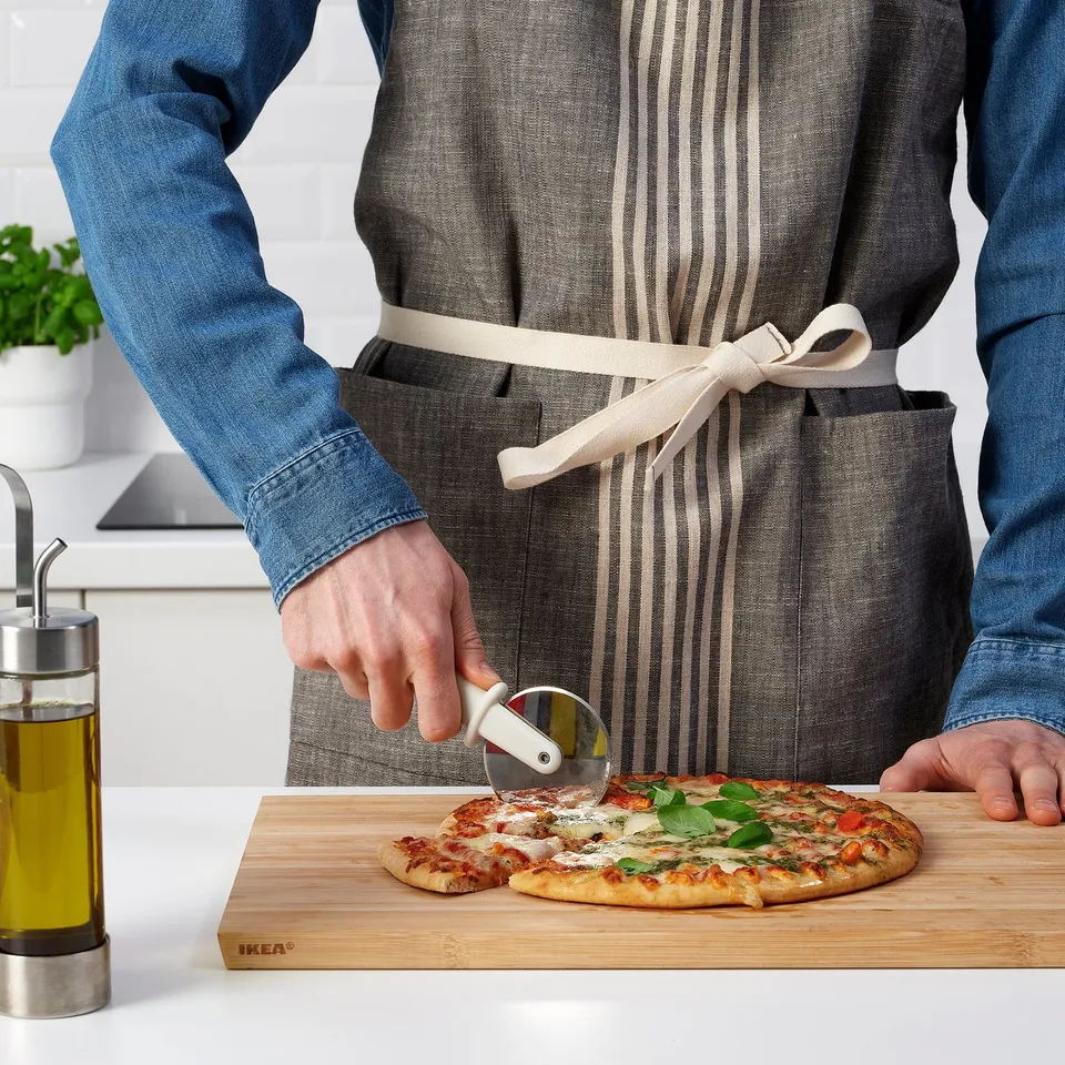 Person slicing pizza using a round cutter on a wooden board in the kitchen.