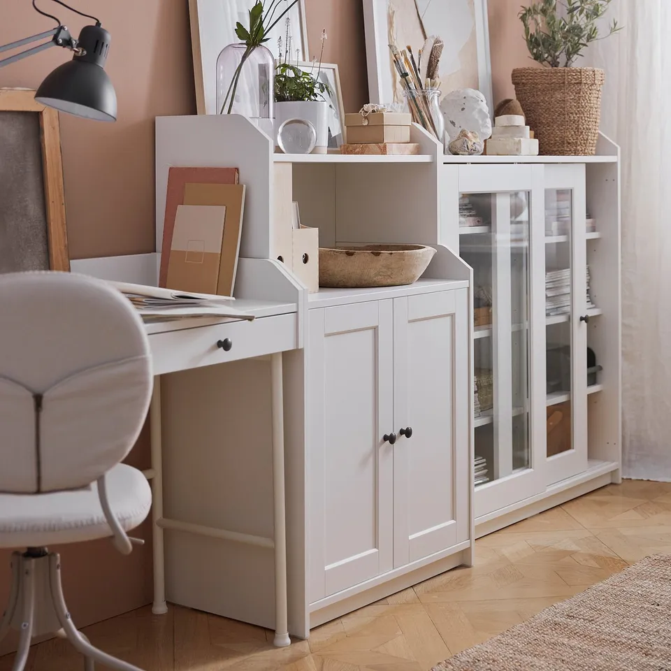 Home office setup: white desk, chair, shelves with plants, lamp.