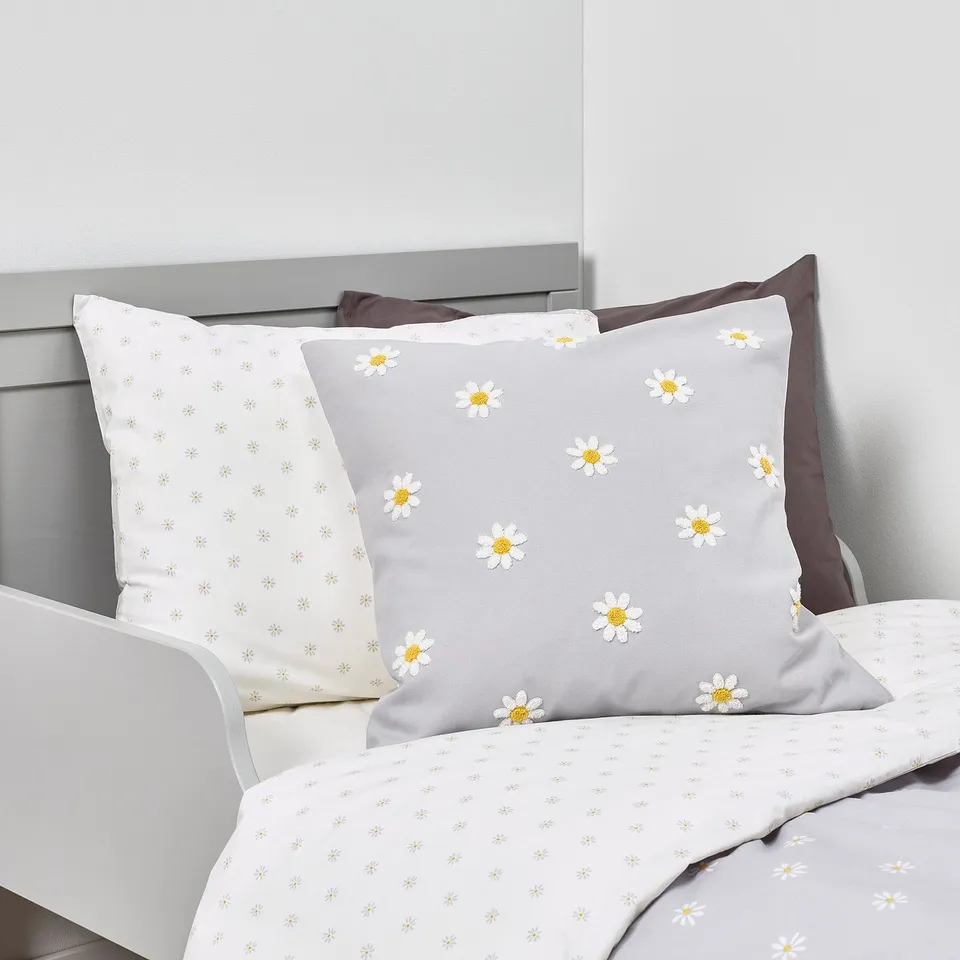 Two pillows on a bed; one white with small flowers, the other grey with large daisies.