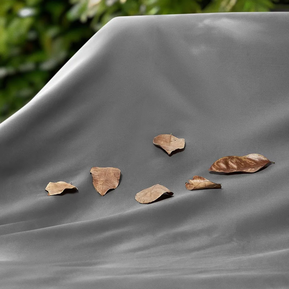 Grey water-resistant outdoor furniture cover with dried leaves on it.