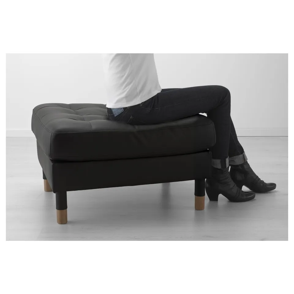 Person sitting on black LANDSKRONA footrest, showing its use as extra seat.