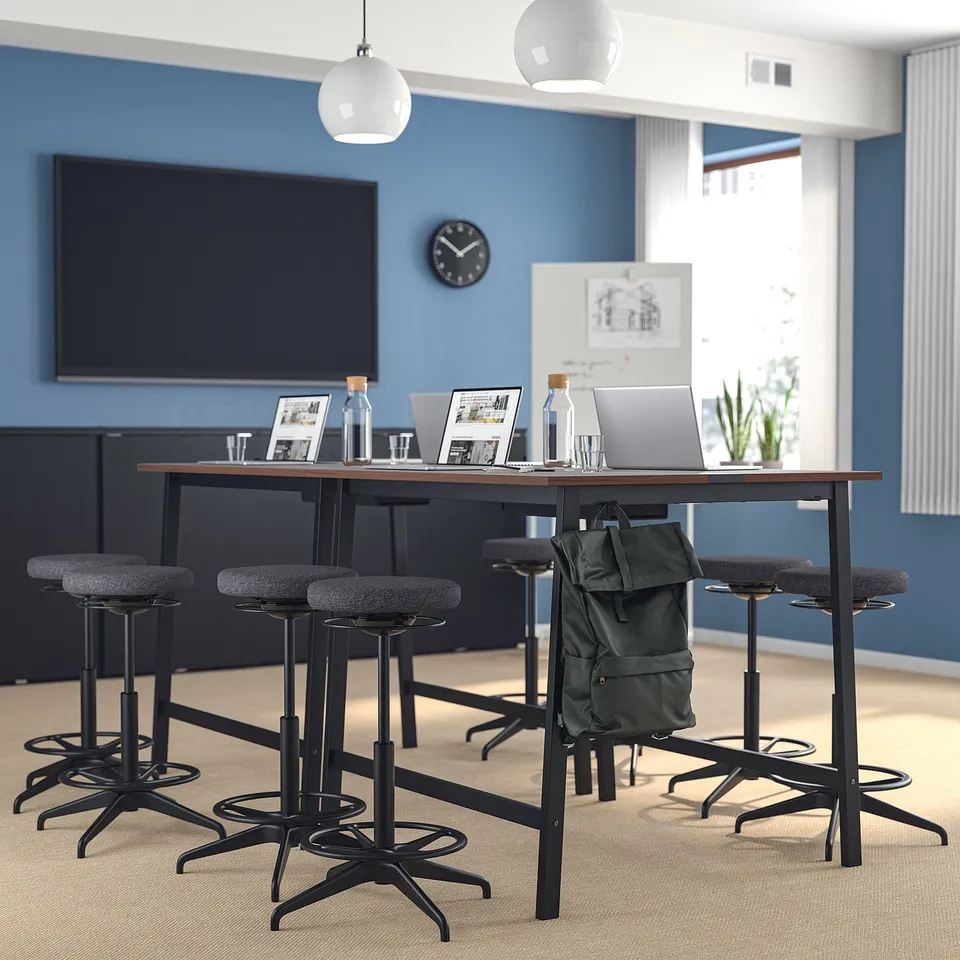 Modern office with MITTZON high table & stools, blue walls, large tv, hanging lights, laptop, plants, bags. Tables & stools are high with footrests.