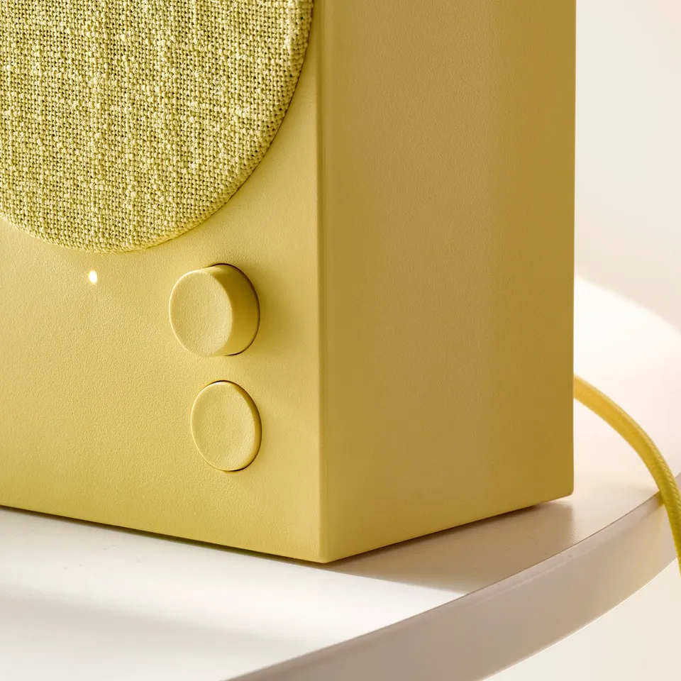 Close-up of a modern, high-quality green bluetooth speaker with smooth controls on a sleek surface.
