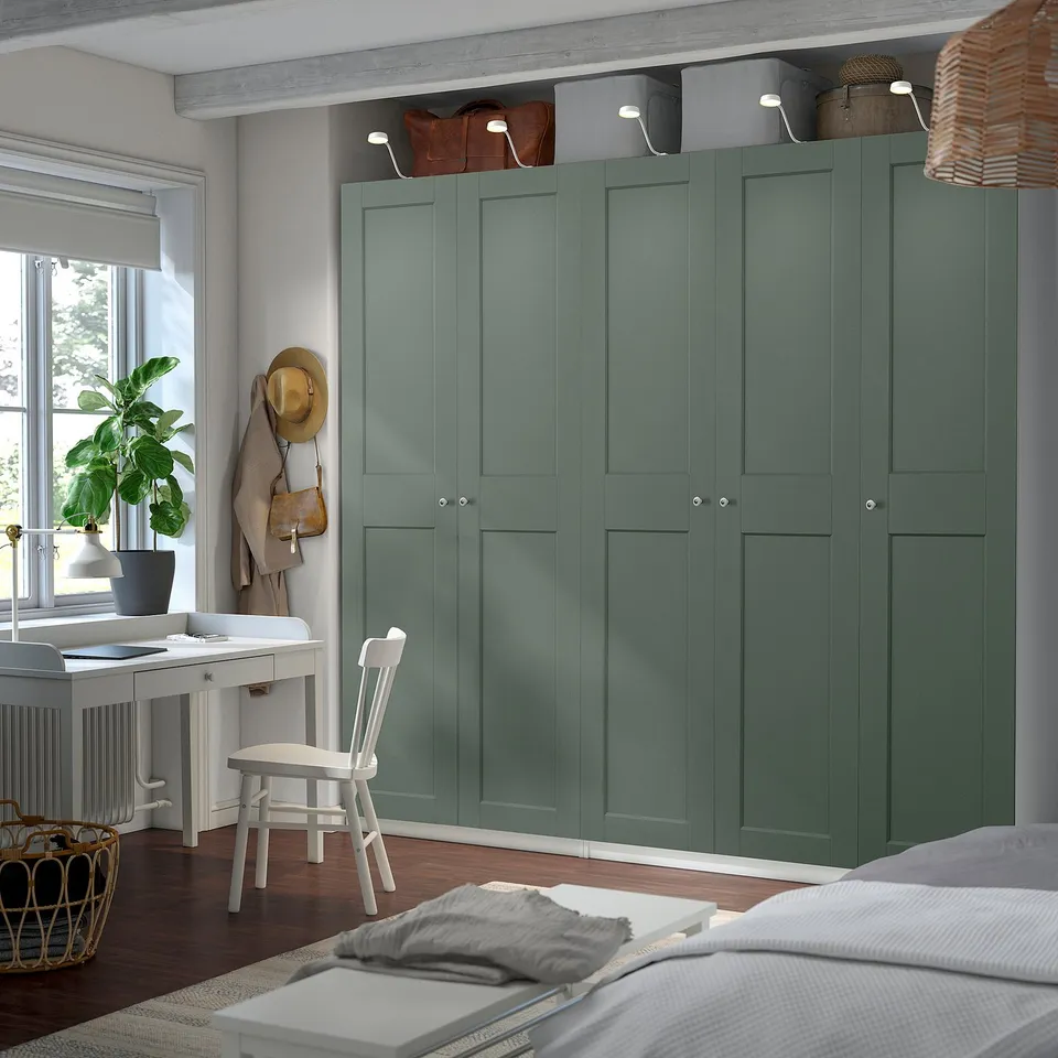 Modern green PAX wardrobe dominates room, spans floor to ceiling, with bags and baskets on top.