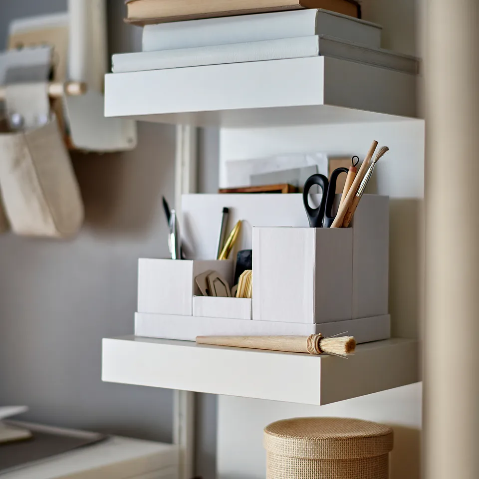 A wall-mounted white LACK shelf unit storing books and stationery in a tidy, minimalist design.