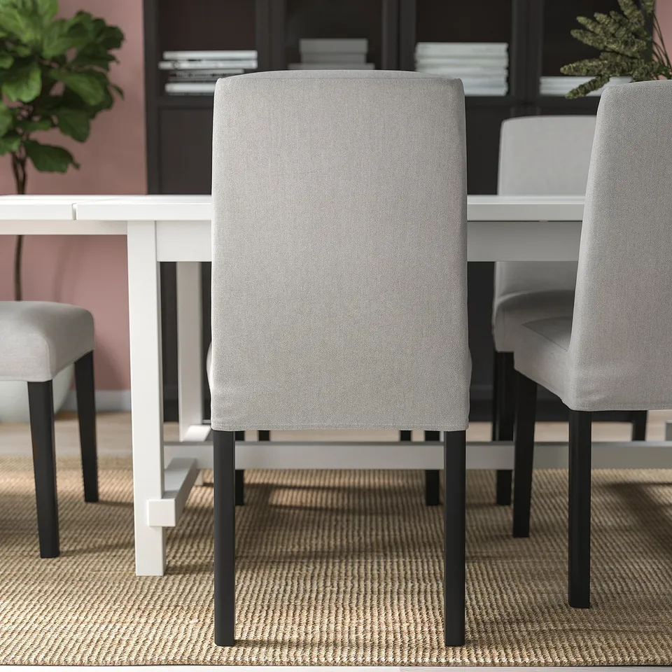 Three modern dining chairs with light grey upholstery and black legs around a white table on a patterned rug.