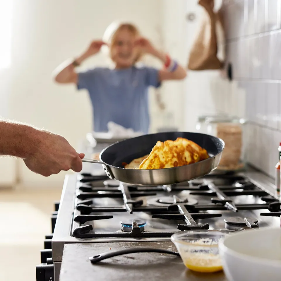 A person cooks in a stainless steel skillet on a gas stove. The non-stick pan is filled with a cooked dish, showcasing an easy-to-clean surface.