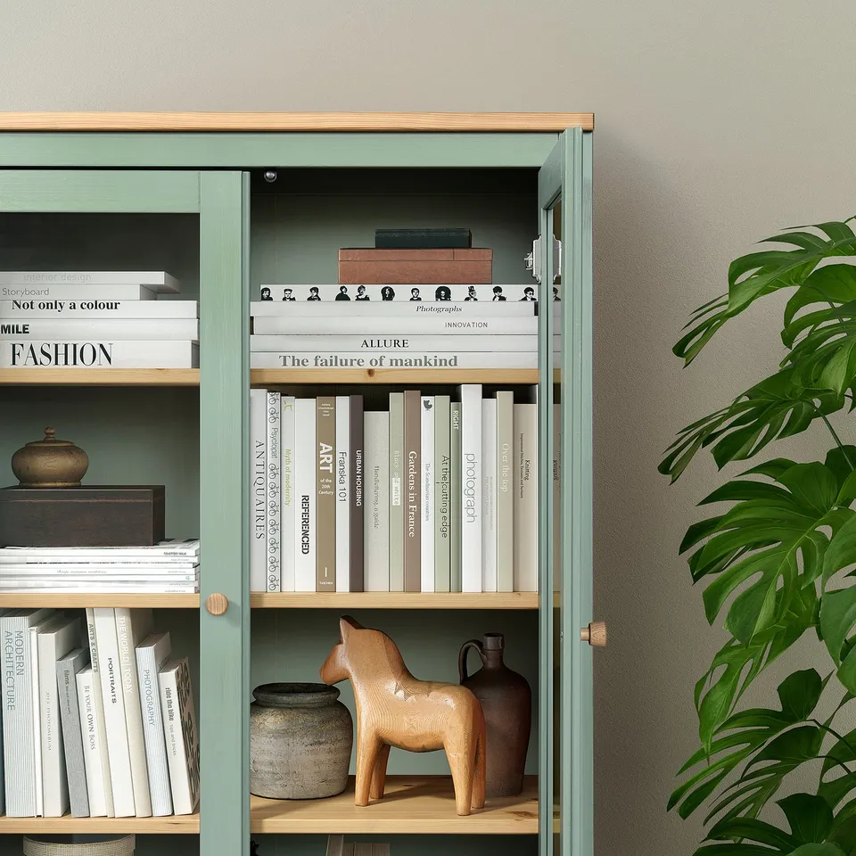 Green glass-door bookshelf with adjustable wood shelves holding books and decor.