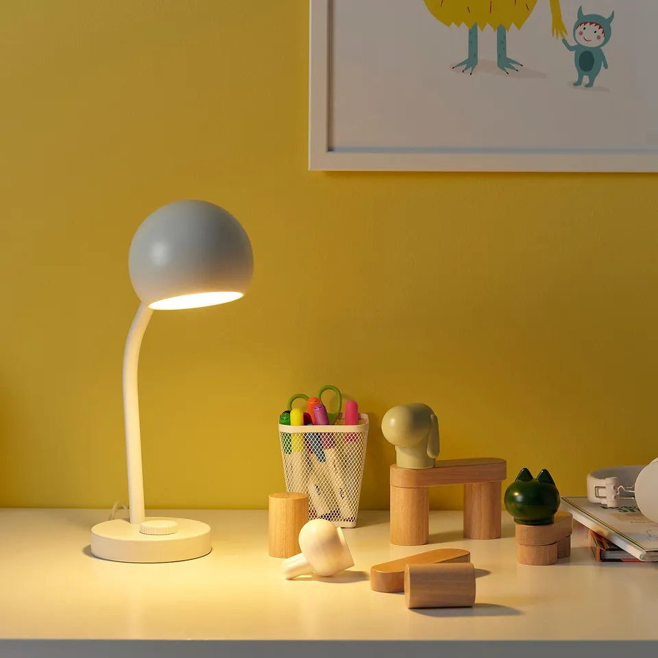 KORVSNÖRE lamp on table, illuminating toys and desk items.