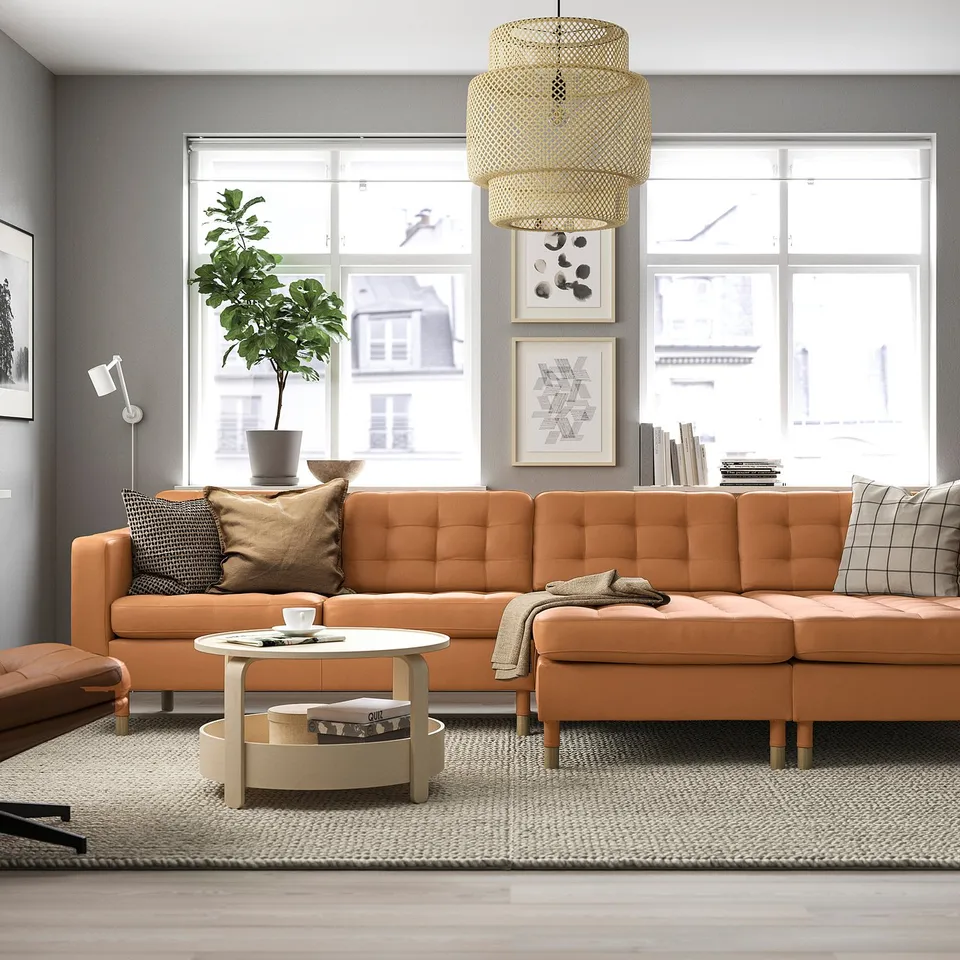 Modern living room with large orange l-shaped sofa, round coffee table, and leafy plant. The sofas big and comfy, taking up most of the space.