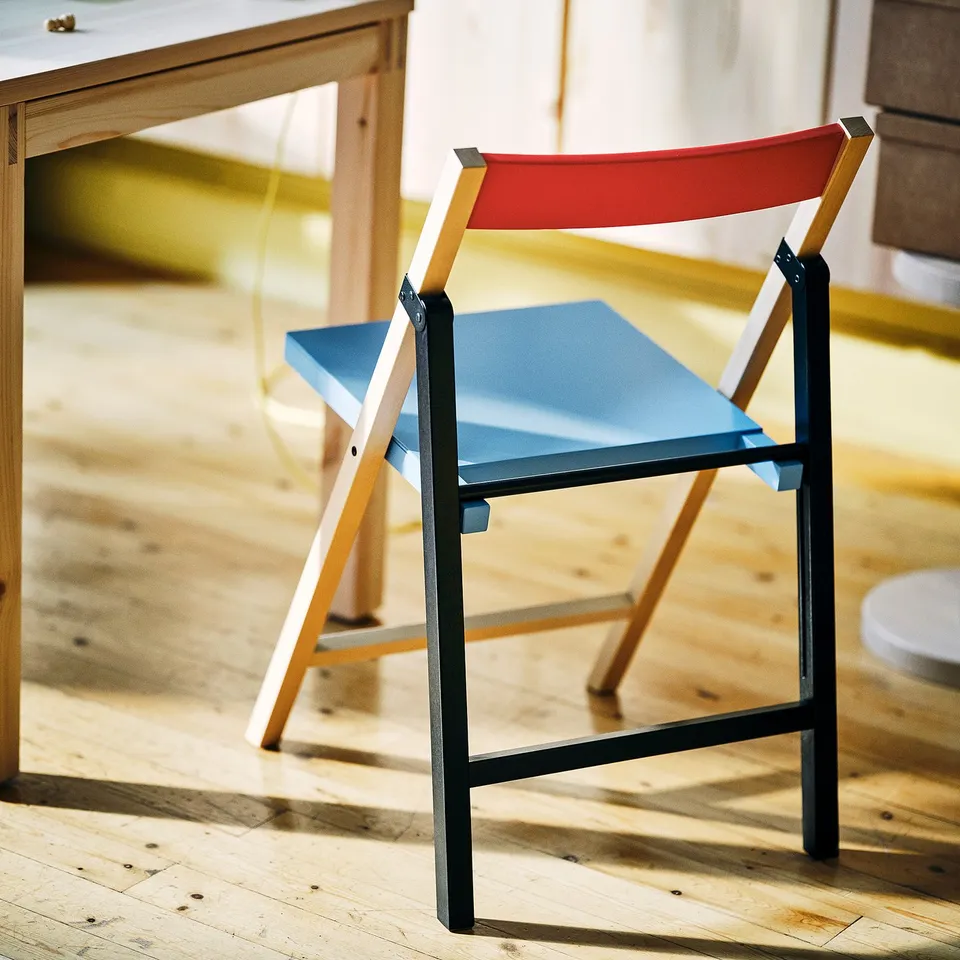 IKEA PS 2026: bright red folding chair with blue seat, wooden frame, compact design.