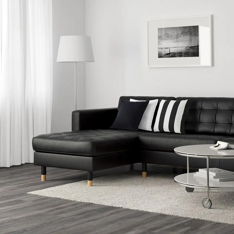 Modern living room with black l-sofa, striped pillows, coffee table, rug, lamp, wall art.