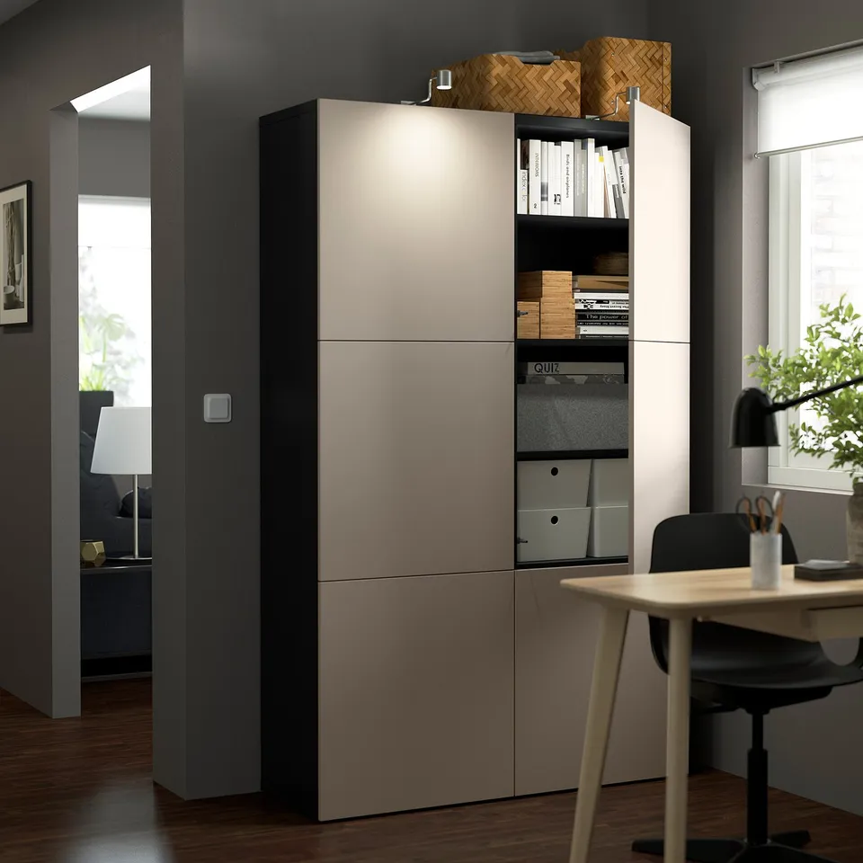 Office setup with BESTÅ unit, desk, chair, and lamp. Window, plant, and another room in background.