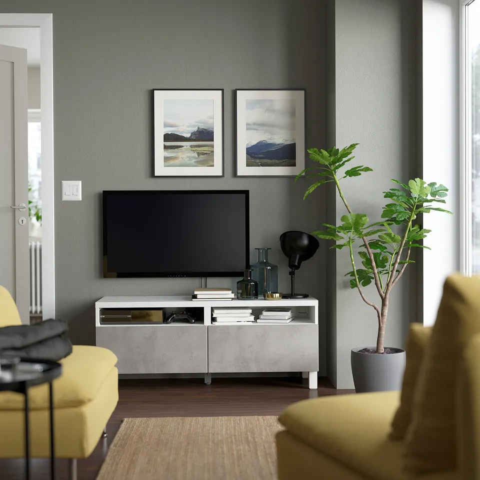 Modern living room with BESTÅ tv bench, flat-screen tv, two yellow armchairs, green plant, and nature photos on wall.