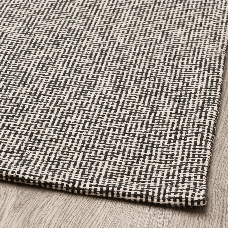 Black and white patterned rug on wooden floor, showcasing intricate weave and high-quality cotton texture.