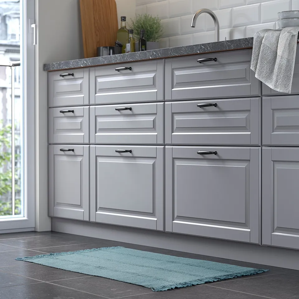 Grey kitchen cabinets with a small blue rug, stainless sink, and decorative items.