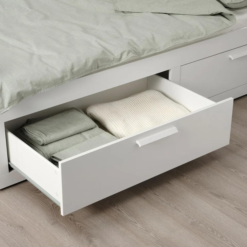 A white BRIMNES daybed with drawers; one drawer open holding folded linens and towels.
