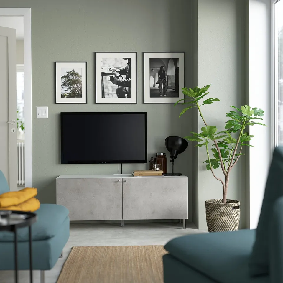 Modern living room: sage walls, blue sofa, grey tv stand, black tv, plants, art, woven coffee table.