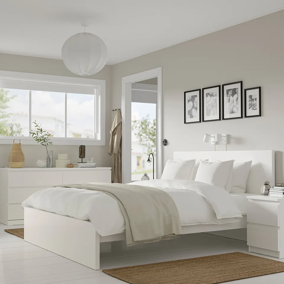 Modern minimalist bedroom with MALM bed, dressers, and nightstands. White linens, photos, candles, and a hanging light.